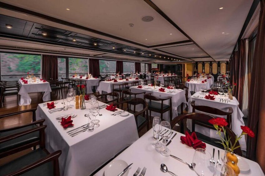 A restaurant with multiple tables set for dining, featuring white tablecloths, red napkins, and glassware. 5