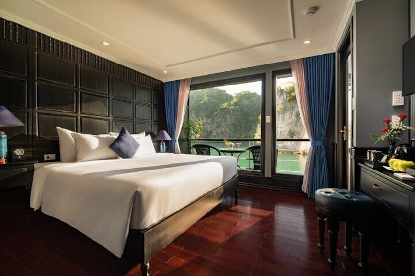 A hotel room with a large bed, dark wood paneling, a balcony with a view of greenery, and a desk with a lamp. 5