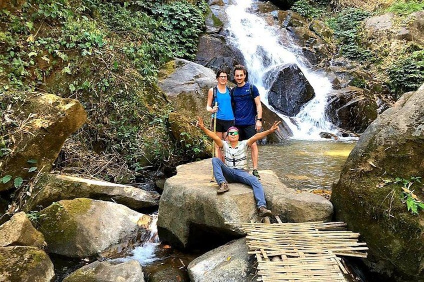 A group of people sitting on rocks by a waterfall in a forested area. 3