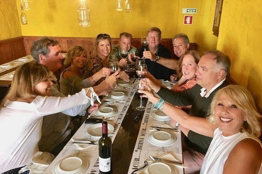 Eine Gruppe von Menschen stoßen in einem Restaurant mit gelben Wänden und Holzvertäfelung an einem langen Tisch an. 4