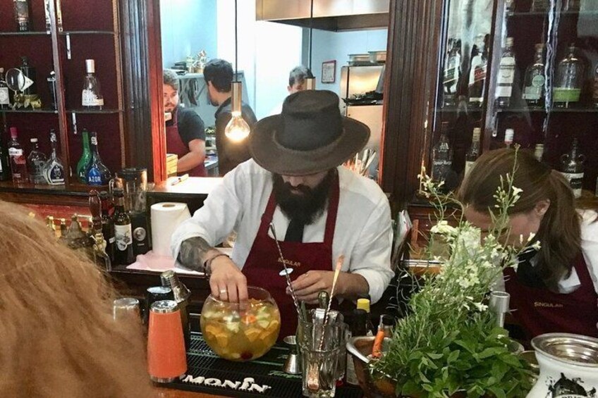 A bartender preparing a drink behind the bar with various bottles and a cash register. 3