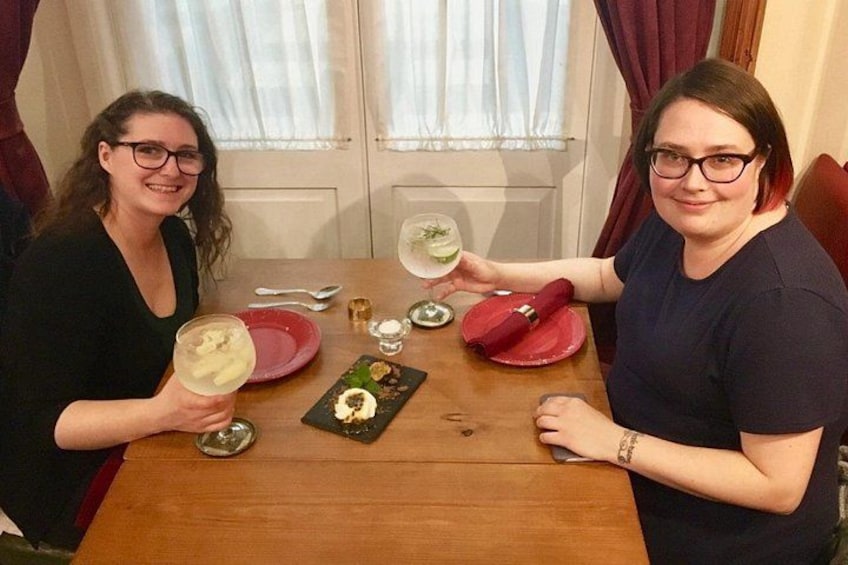 Dos personas sentadas en una mesa de madera con platos, vasos y un pequeño recipiente de comida. 3