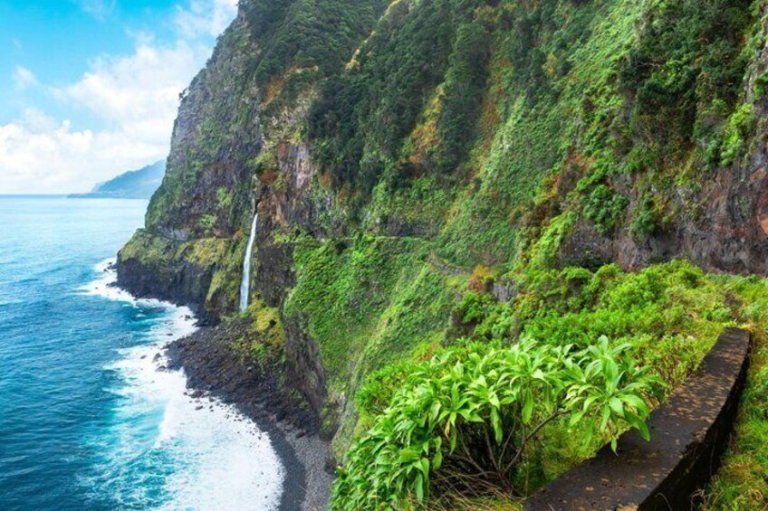 Une falaise côtière avec une cascade, une végétation luxuriante et un sentier étroit. 2