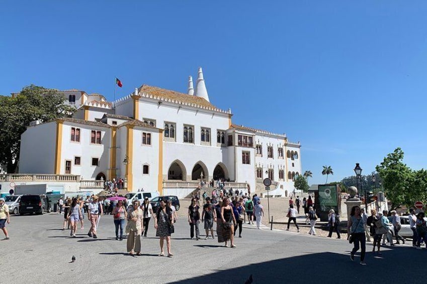 A historic white building with arches and a clock tower, surrounded by a crowd of people. 1