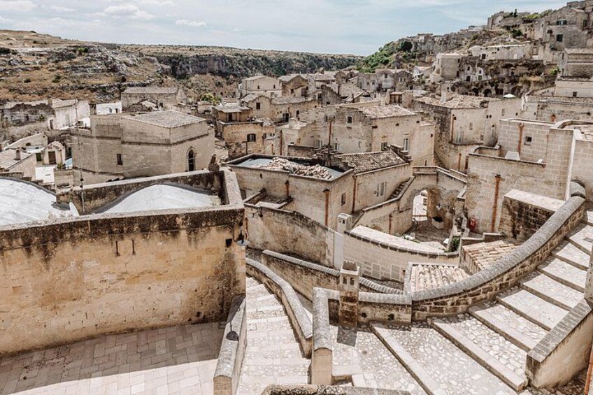 A historic town with stone buildings, a central courtyard, and a hilly backdrop. 2