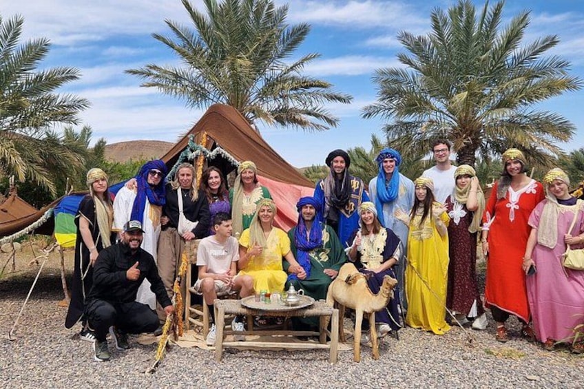 Een groep mensen in traditionele kleding poseert voor een tent, met palmbomen op de achtergrond. 3