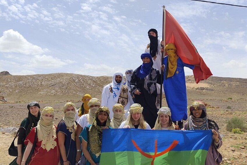 Een groep mensen in traditionele kleding houdt een vlag vast in een woestijnlandschap. 2