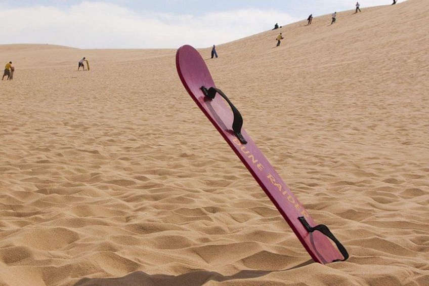 A pink snowboard on a sandy dune with people in the background. 4