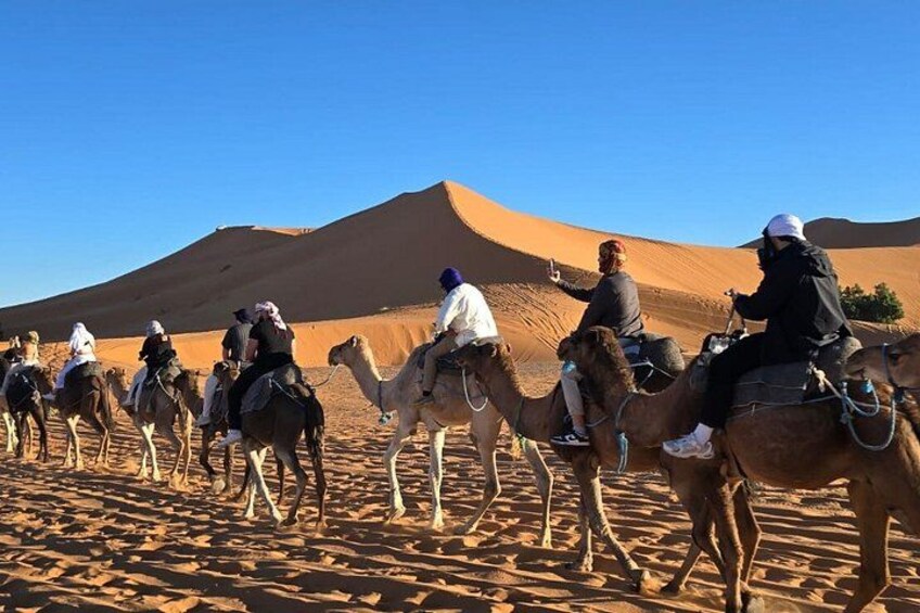 A group of people riding camels across a desert landscape with sand dunes in the background. 3
