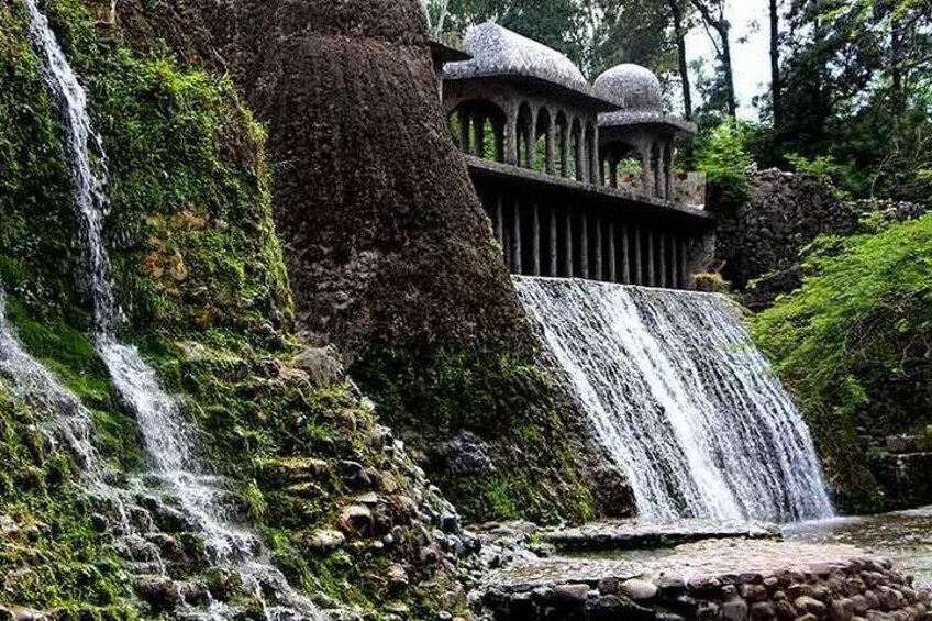 Una cascada que se precipita sobre rocas cubiertas de musgo, con una estructura tradicional al fondo. 3