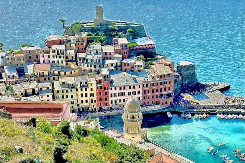 A coastal town with colorful buildings, a prominent tower, and a fortified structure overlooking the sea. 5