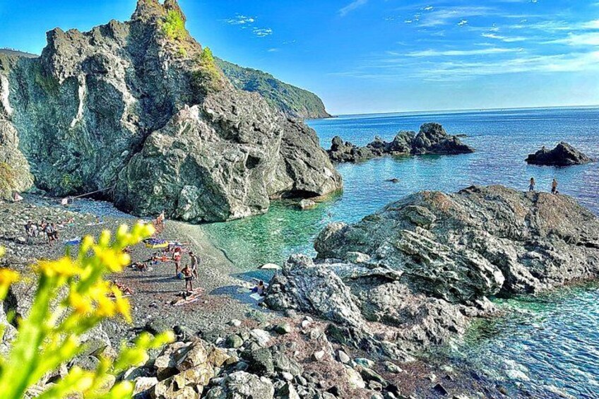 A rocky coastline with clear blue water, large boulders, and a few people. 2