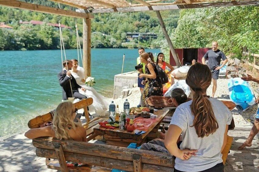 Eine Hochzeitszeremonie am See mit einer Holzliege, Gästen und einem Buffet. 3