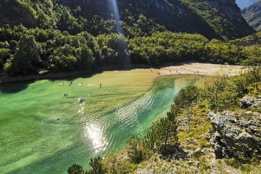 Ein klarer See, umgeben von Bergen, mit einem Sandstrand und badenden Personen. 4