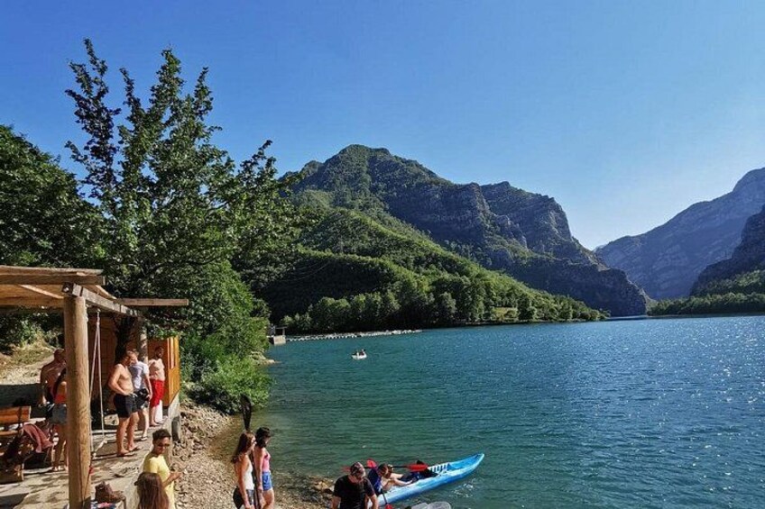 Ein See mit einer Holzsteganlage, Personen in der Nähe des Wassers und Bergen im Hintergrund. 5