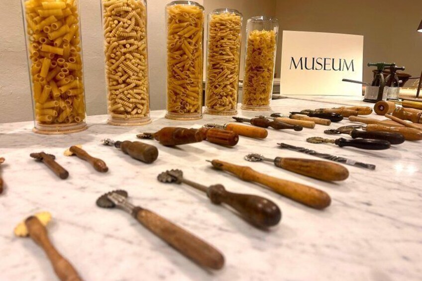 Pasta and pasta-making tools displayed in glass containers on a marble surface. 5