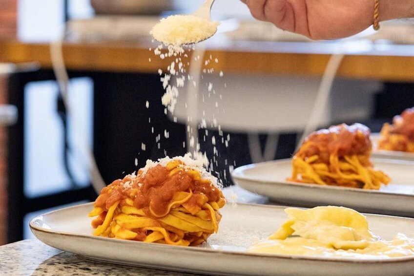Une personne saupoudrant du fromage râpé sur une assiette de spaghettis. 3