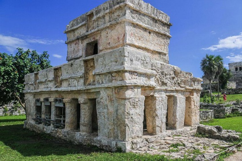 A stone pyramid structure with columns and a stepped design, surrounded by grass and trees. 5