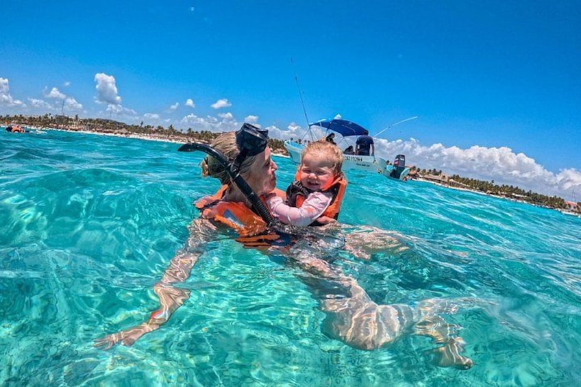 A person snorkeling with a child in clear turquoise water, a boat in the background, and a distant shoreline. 4