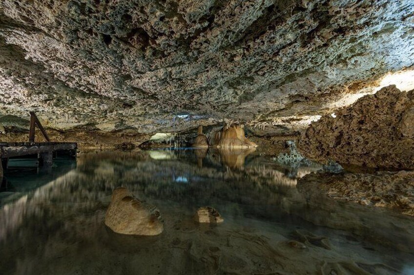 A cave interior with stalactites, stalagmites, and a reflective water surface. 3