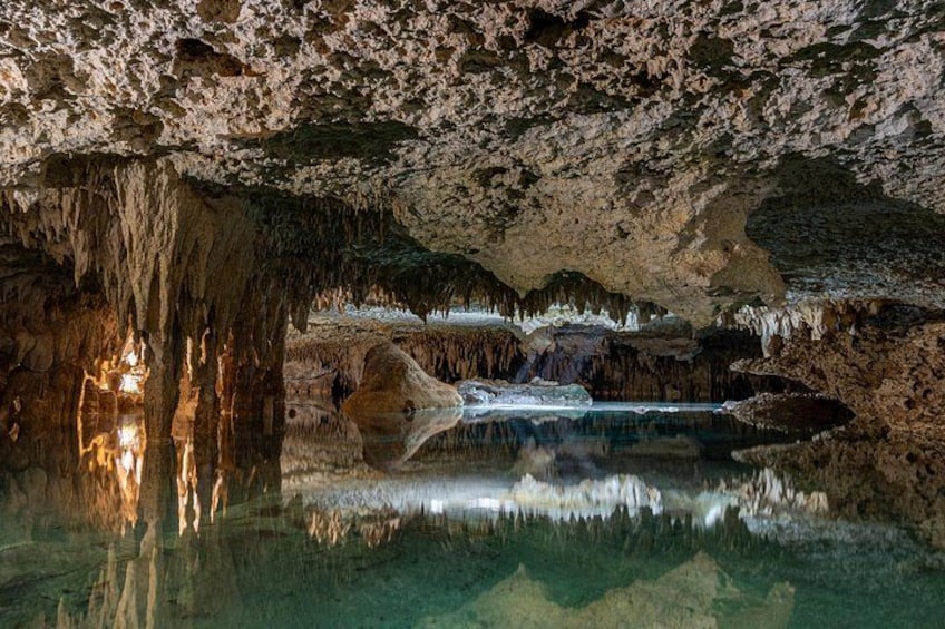 A cave with stalactites, stalagmites, and a reflective water pool. 5