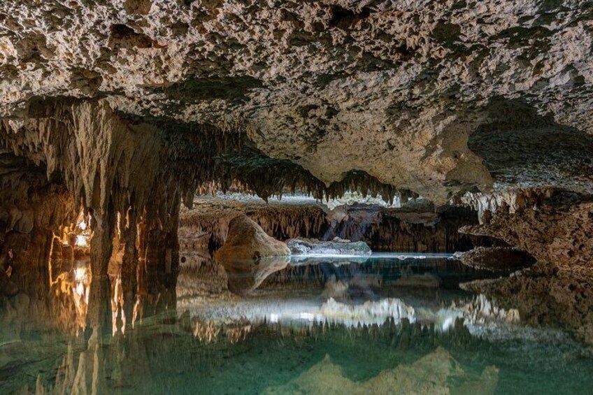 A cave with stalactites, stalagmites, and a reflective water pool. 2