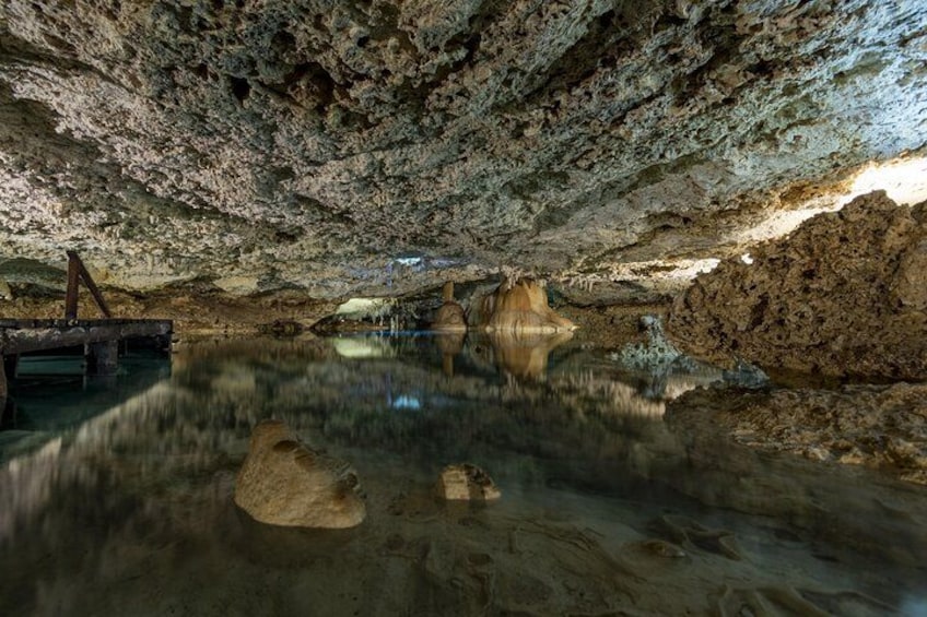 A cave interior with stalactites, stalagmites, and a reflective water surface. 5