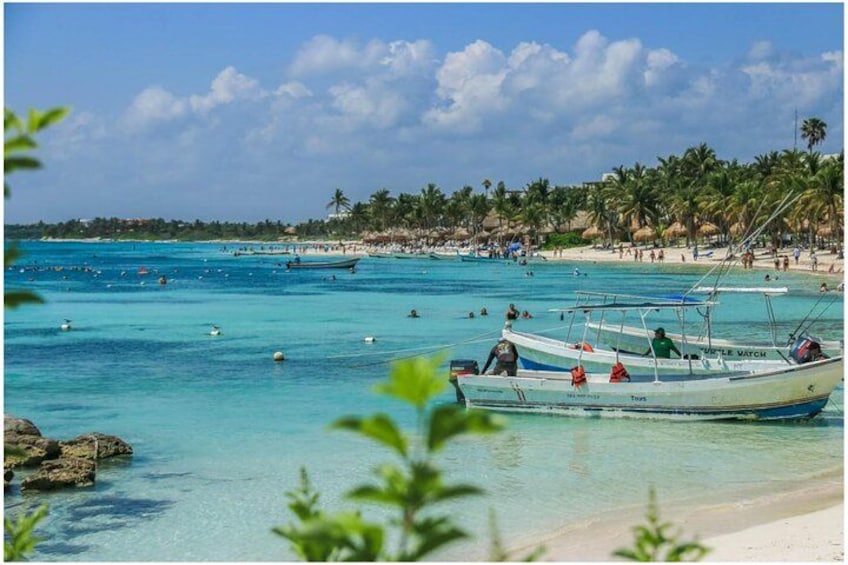 A beach with clear turquoise water, boats, and palm trees. 4