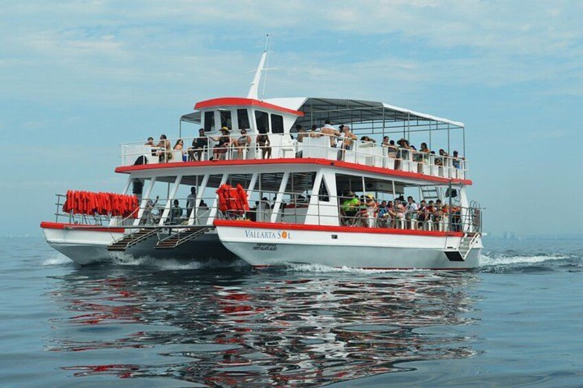 A white and red boat with passengers on deck, moving through calm water. 4