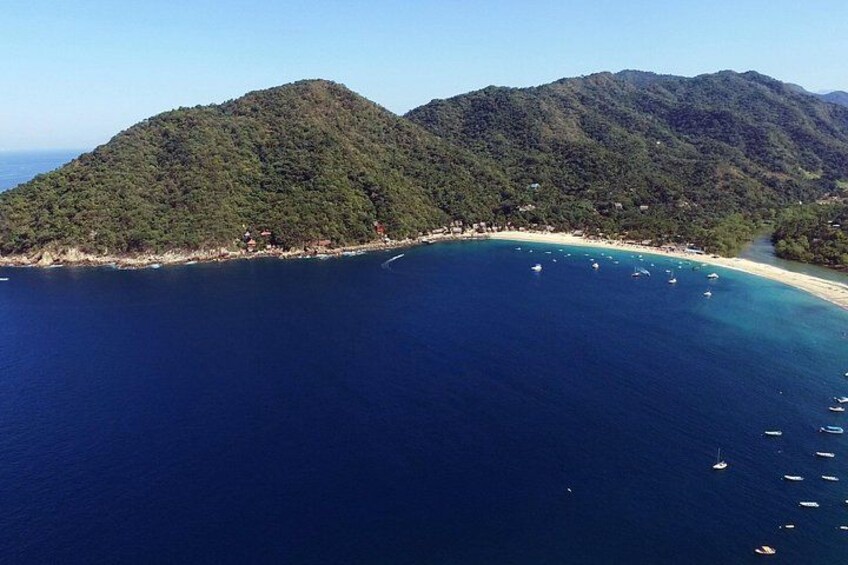 A coastal landscape with a clear blue sea, a sandy beach, and lush green hills. 3