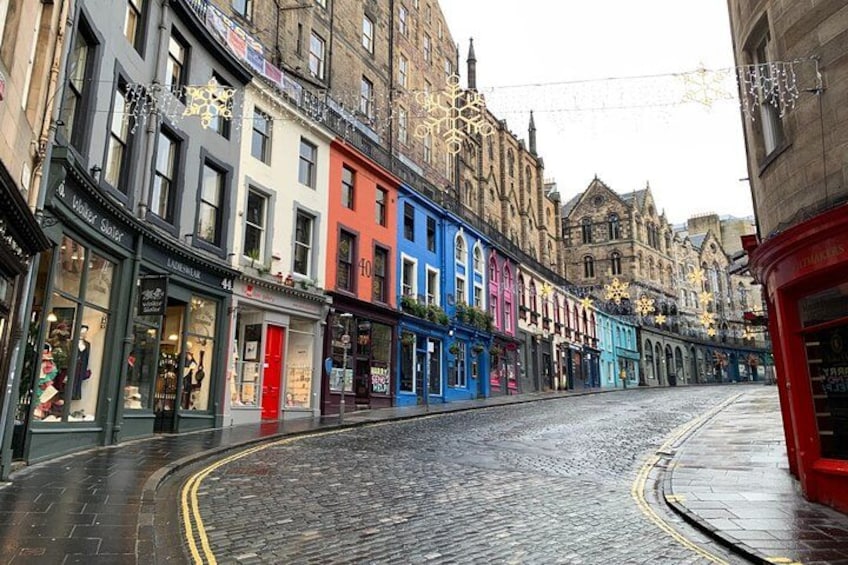 A cobblestone street lined with colorful buildings, a red bus, and snowflakes hanging above. 2
