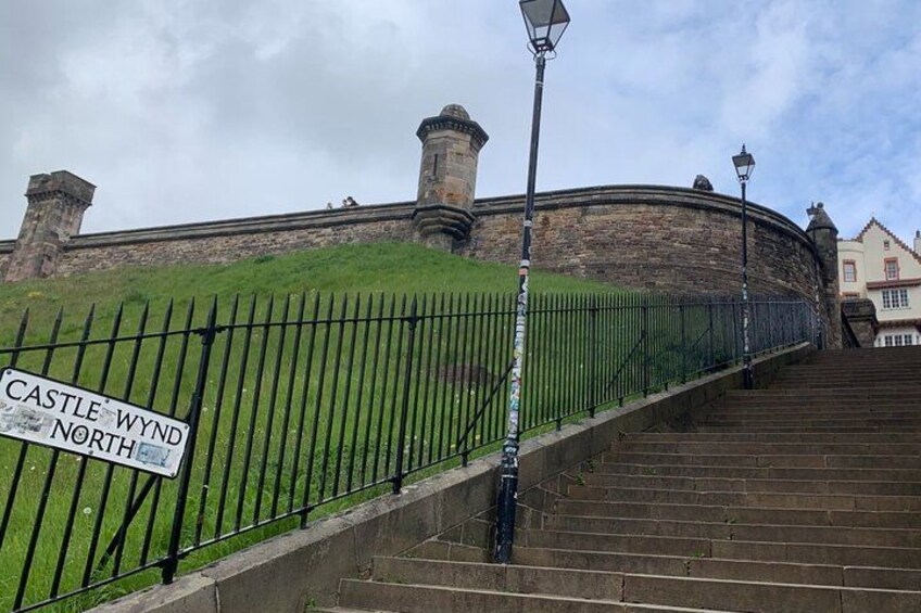 A stone wall, a sign reading 'Castle Wynd North', and a staircase leading up to the wall. 4