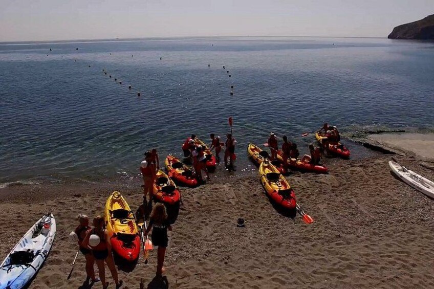 Een strand met op een rij geparkeerde kajaks en mensen die zich voorbereiden om te kajakken. 4