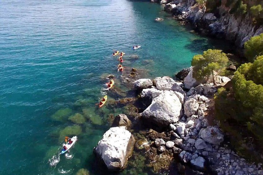 Eine Küstenlandschaft mit klarem türkisblauem Wasser, felsigen Ufern und einigen Personen, die sich an Wassersportaktivitäten beteiligen. 5