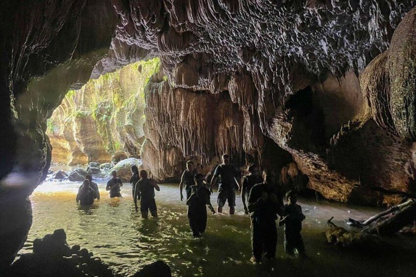 Een grot met stalactieten en stalagmieten, mensen die door water lopen, en een natuurlijke rotsformatie. 5