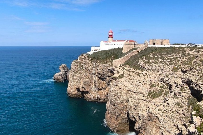 A coastal landscape with rocky cliffs, a lighthouse, and a fortified building. 1