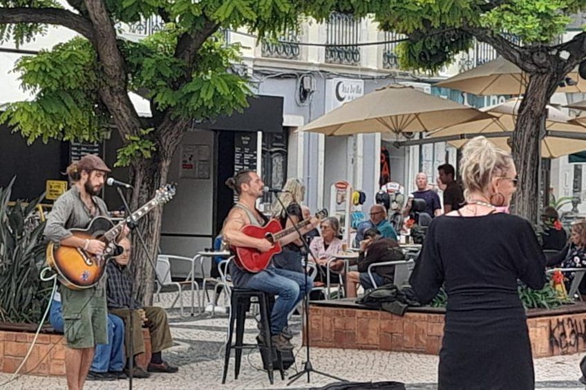 A street musician playing guitar, seated on a chair, with a microphone stand in front. 2