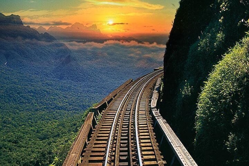 A railway track curving along a steep mountain ridge with a sunset in the background. 1