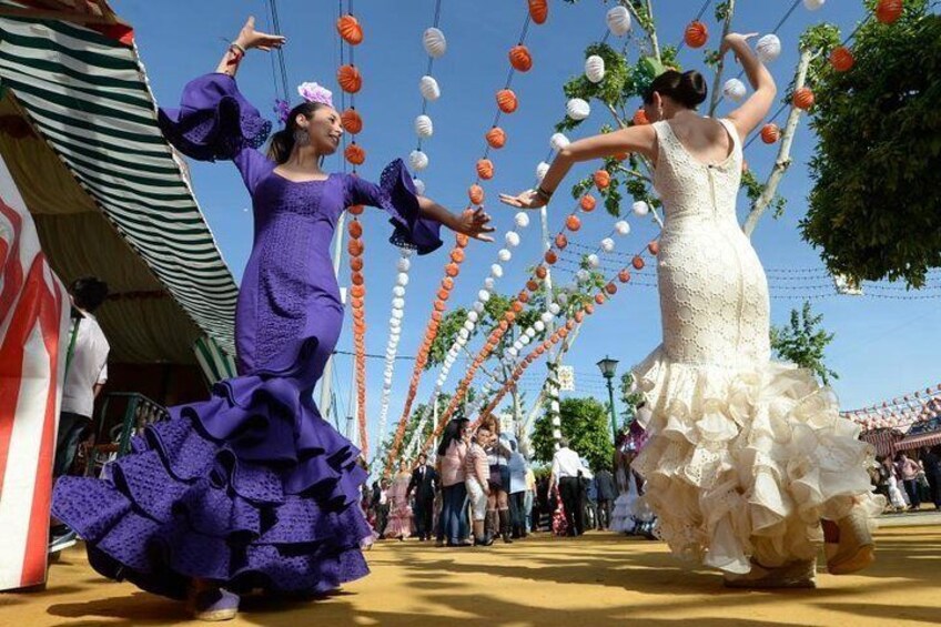 Two women in traditional dresses dancing in a festive outdoor setting with hanging decorations. 2