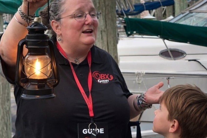 A person holding a lantern, wearing a black shirt with logos, standing outdoors near boats. 4