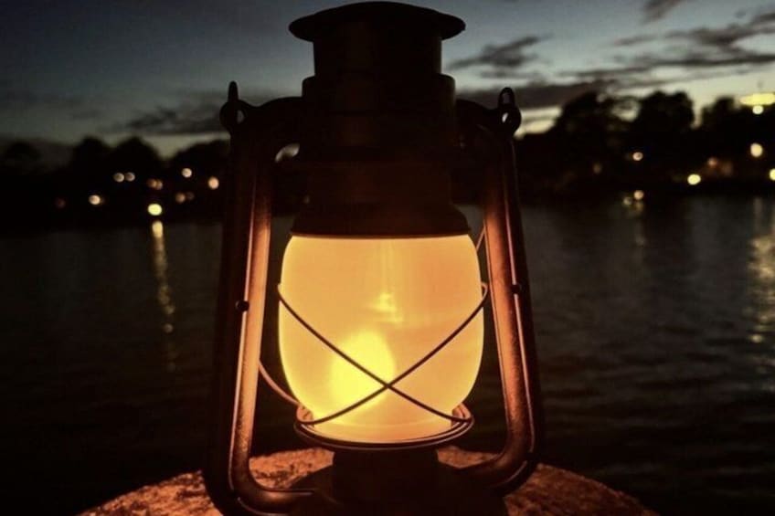 A lantern with a glowing light, placed on a rock by a body of water at dusk. 2