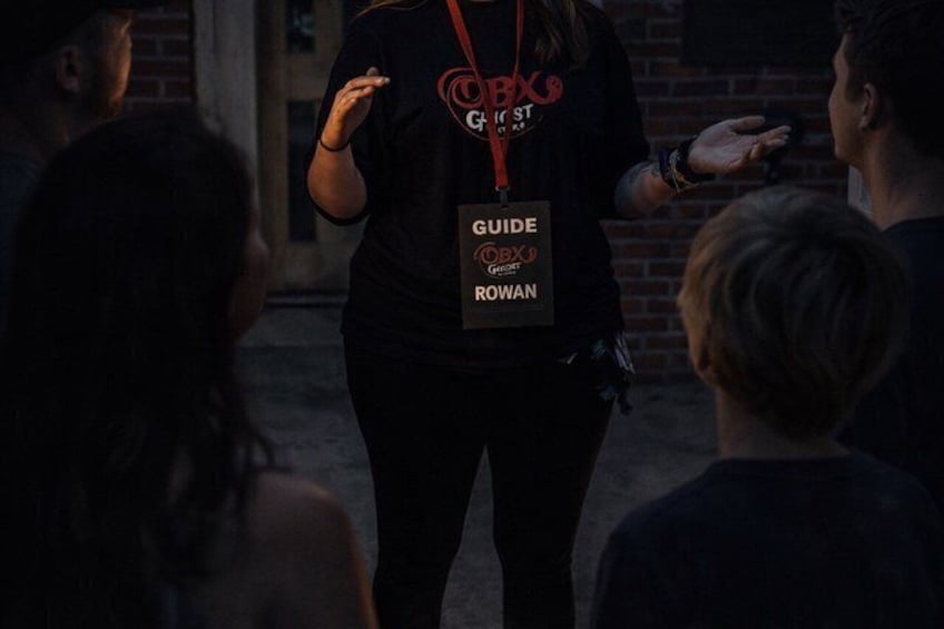 A person wearing a black shirt with a 'GUIDE' badge and 'ROWAN' text, standing in front of a group of people. 3