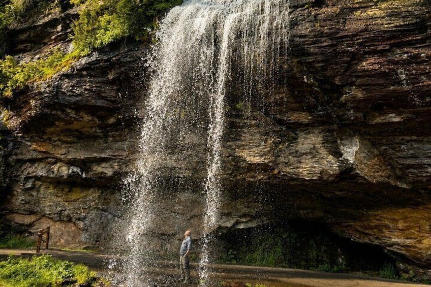 A waterfall cascading down a rocky cliff with a person standing at the base. 5