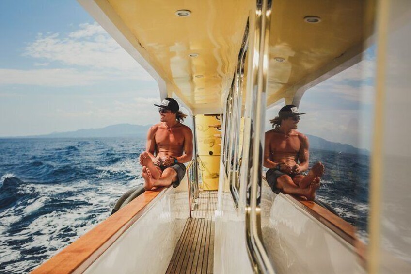 A person sitting on a boat deck with a view of the ocean and mountains in the distance. 2