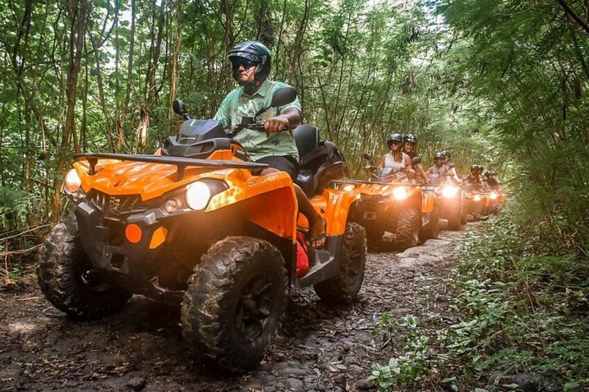 A group of orange all-terrain vehicles on a muddy forest trail. 2