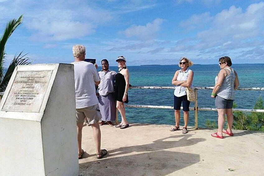 A group of people standing by a coastal walkway with a plaque, ocean, and clear sky. 3