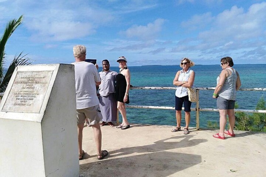 A group of people standing by a coastal walkway with a signboard, overlooking the ocean. 3