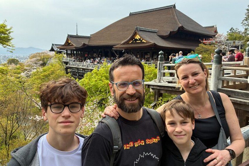 Una familia de cuatro personas frente a un edificio japonés tradicional, con flores de cerezo al fondo. 1