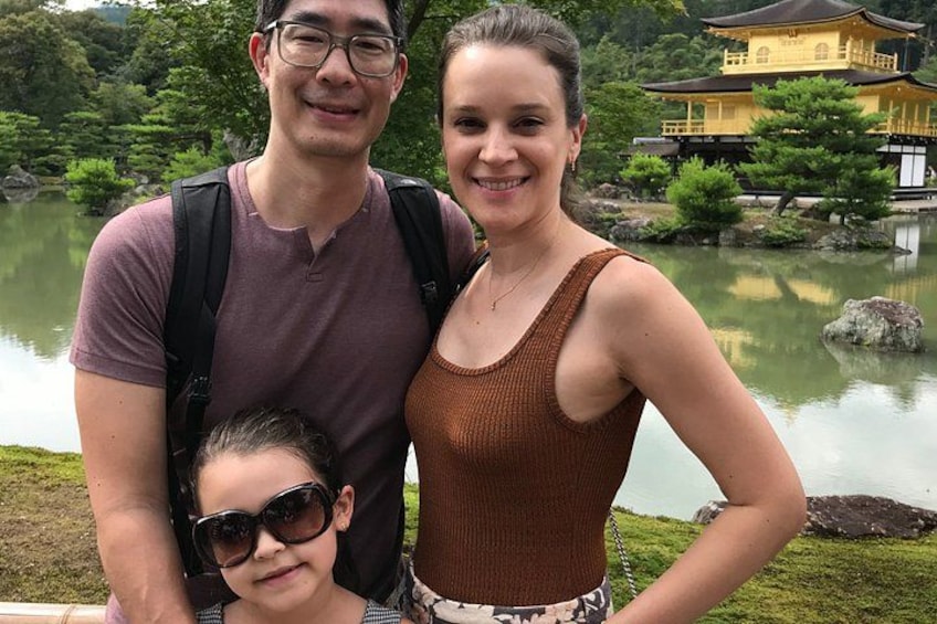 Una familia de tres personas frente a un estanque, con un edificio tradicional al fondo. 2