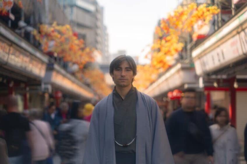 Eine Person in traditioneller Kleidung geht eine von Herbstlaub gesäumte Straße entlang. 1